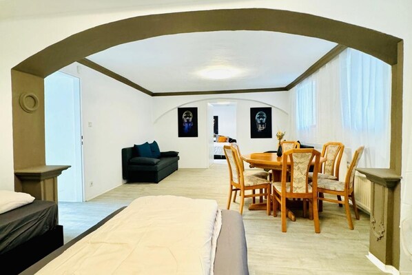 A room with a bed, a dining table with chairs, a sofa, and two framed pictures on the wall.