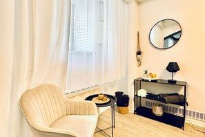 A room with a chair, a small table, a mirror, a shelf with items, and a window with curtains. - Comfortable 2-BR Apt. Stay for 7 Guests – Value (Vienna)