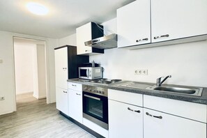 A modern kitchen with white cabinets, a built-in oven, a microwave, and a stainless steel sink.