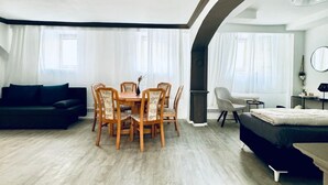 A modern living room with a dining table, chairs, a sofa, and a bed.