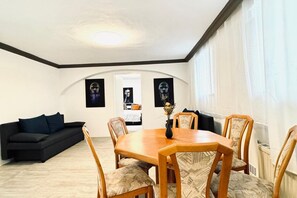 A dining area with a wooden table and chairs, a black sofa, and two framed pictures on the wall.