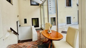 A balcony with a wooden table, two chairs, and a vase with flowers.