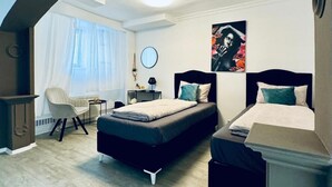 A bedroom with two beds, a chair, a bedside table, a mirror, and a painting on the wall.