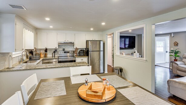 A modern kitchen with white cabinets, stainless steel appliances, and a dining area with a wooden table and white chairs. - Stay & Play in Plymouth: Spacious Home w/ Yard (Plymouth)