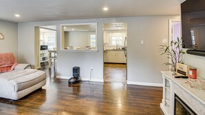 A spacious living area with hardwood flooring, a sofa, a fireplace, and a kitchen visible through an open doorway. - Stay & Play in Plymouth: Spacious Home w/ Yard (Plymouth)