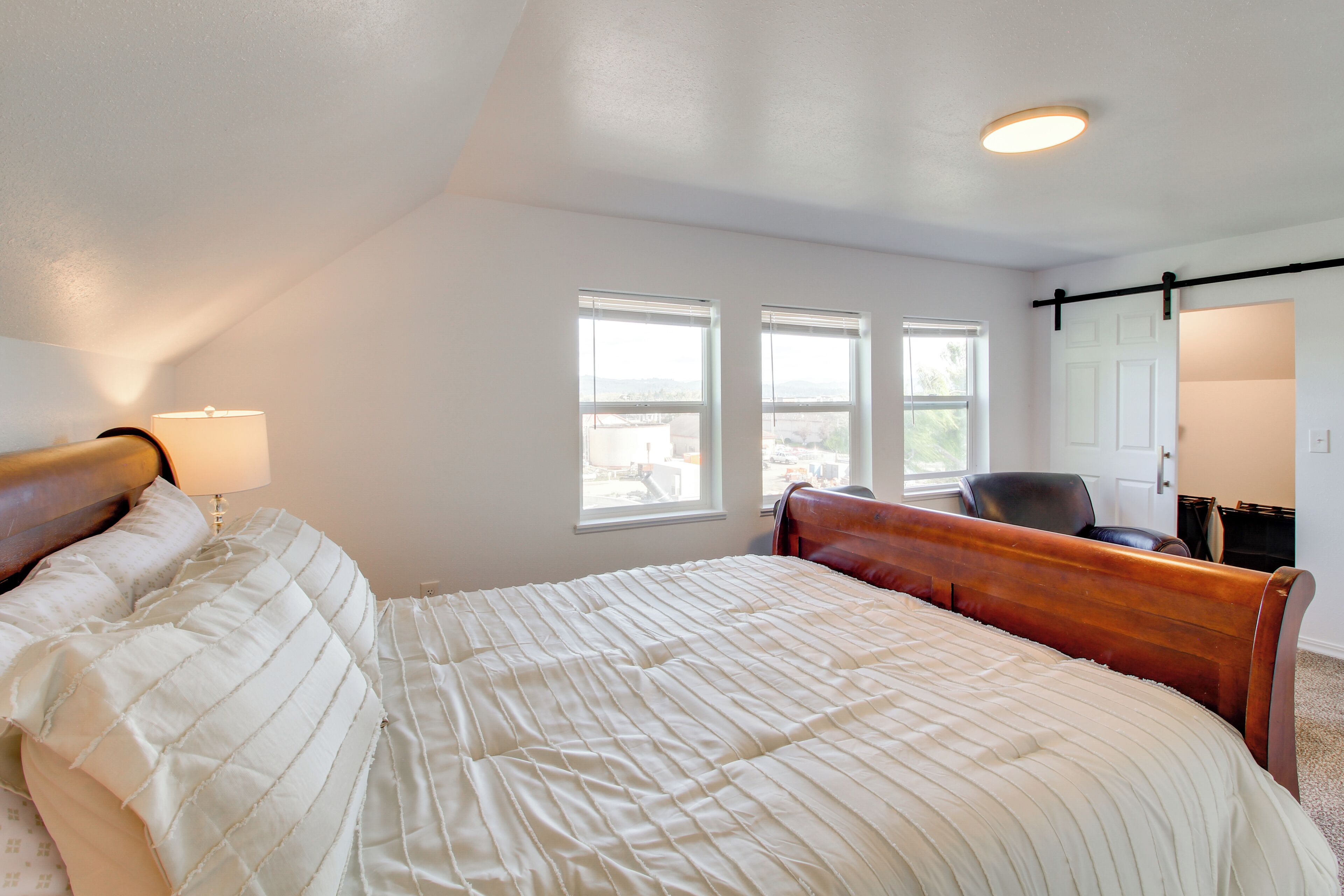 A bedroom with a large bed, a desk, and two windows.