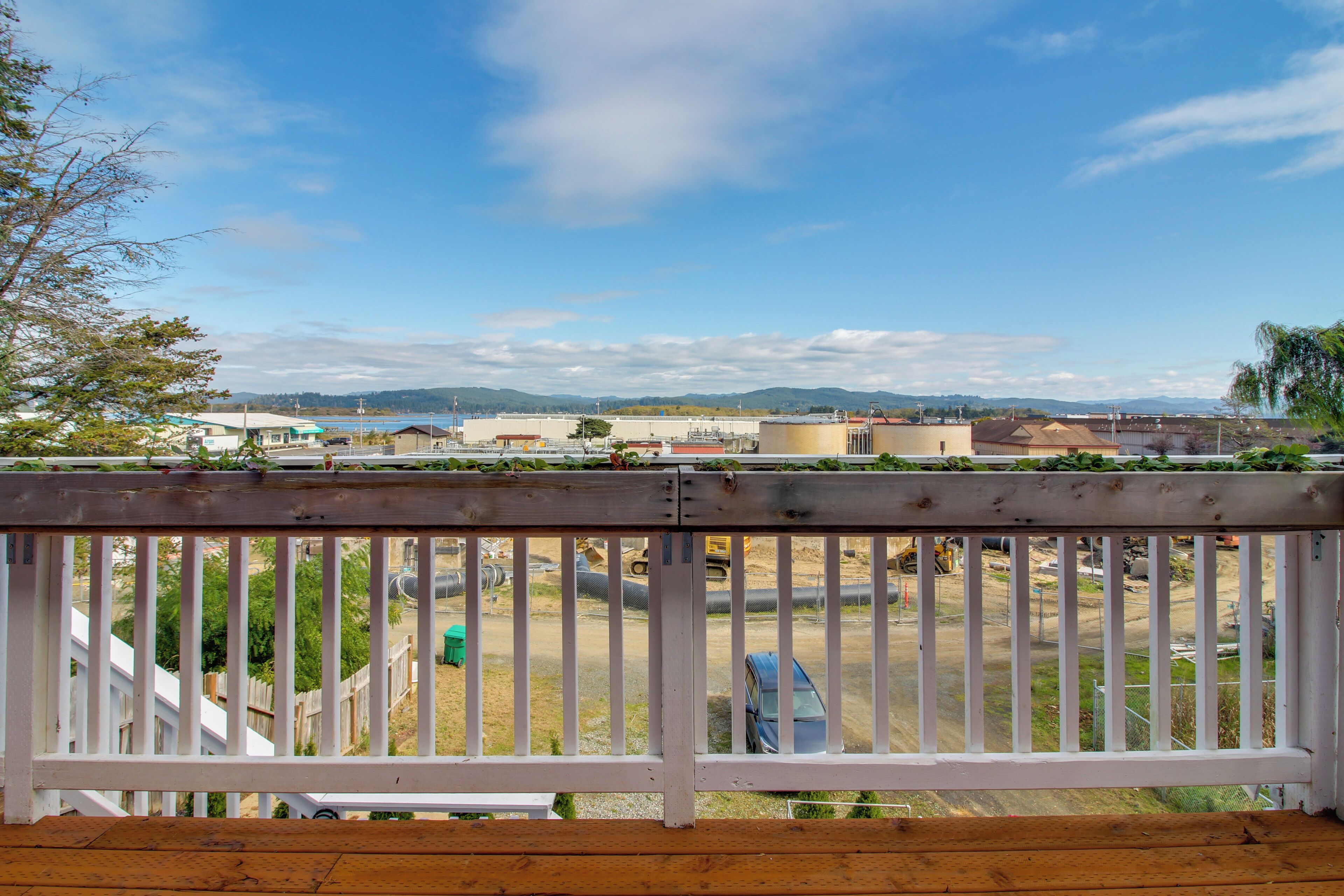 Une terrasse en bois avec une balustrade blanche donnant sur un chantier de construction où l’on aperçoit des bâtiments et un ciel dégagé.