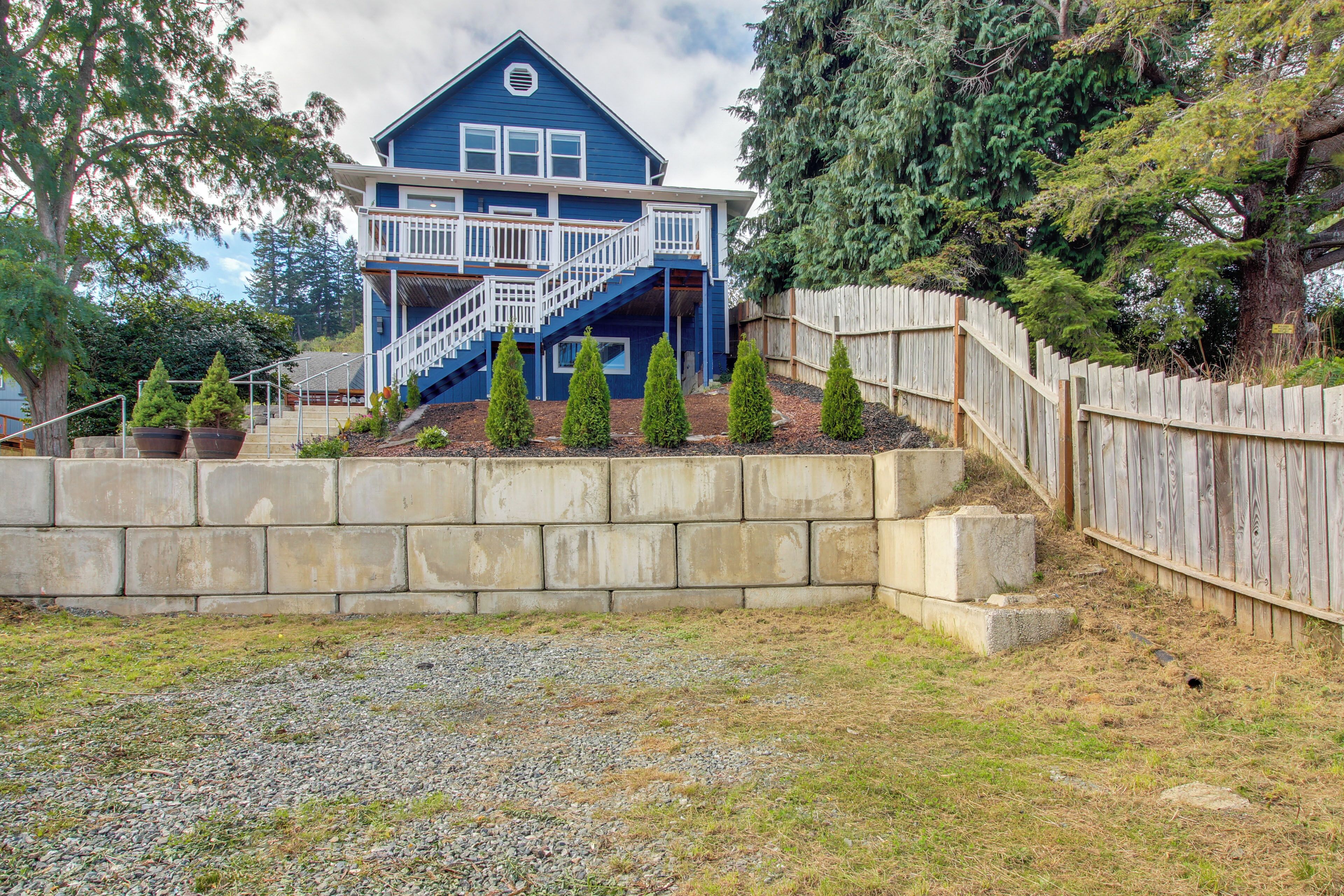 A two-story house with a blue exterior, a wooden deck, and a stone retaining wall.