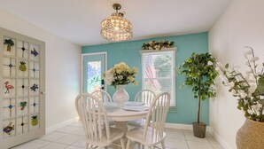 A dining area with a white table and chairs, a vase with flowers, and a potted plant.