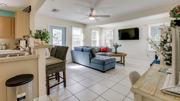A spacious living area with a large sofa, a dining table, and a kitchen area with cabinets and a TV.