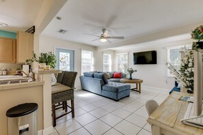 A spacious living area with a large sofa, a dining table, and a kitchen area with cabinets and a TV. - 3 Mi to Jensen Beach: Pet-friendly Getaway w/ Yard (Jensen Beach)