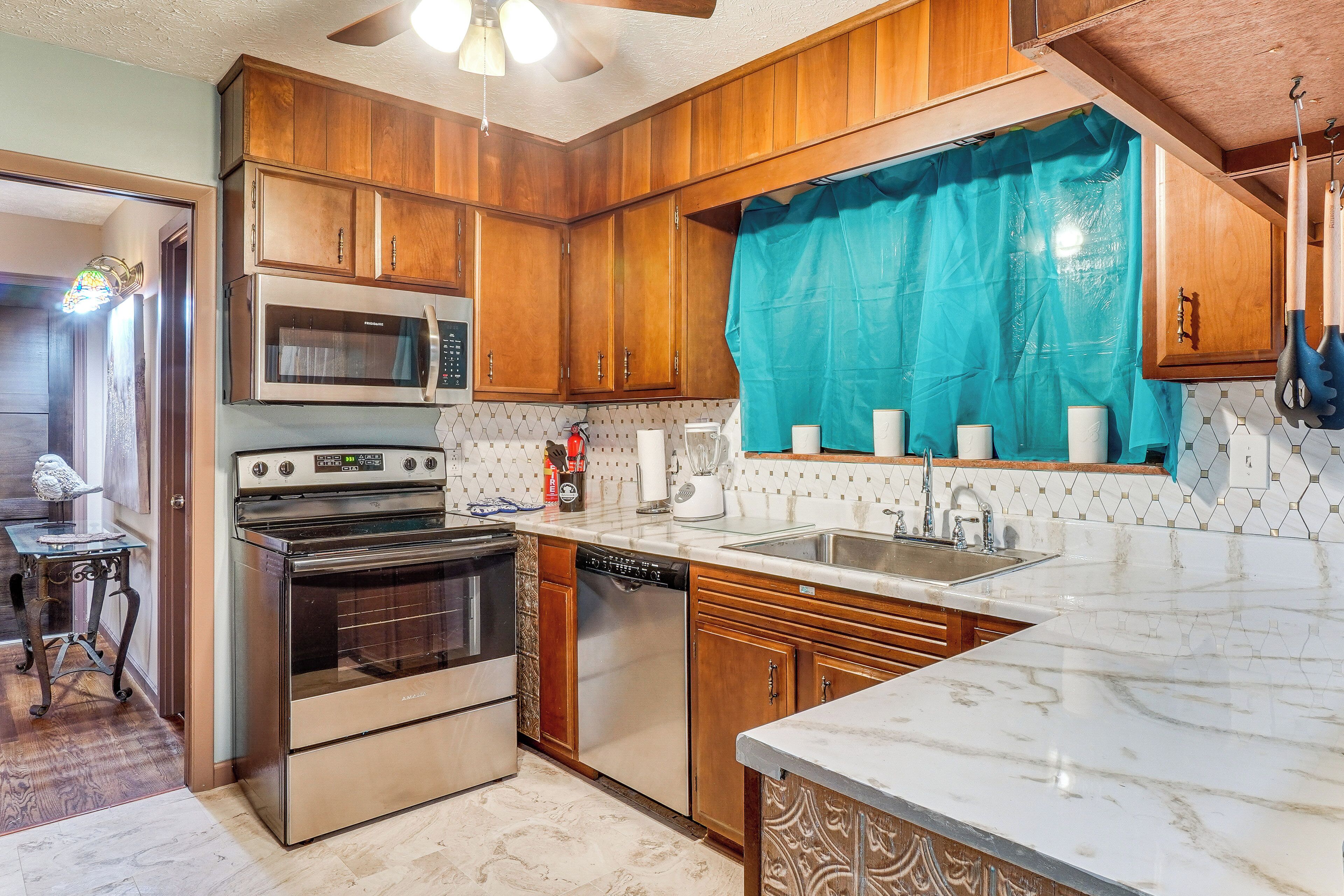 A kitchen with wooden cabinets, stainless steel appliances, a tiled backsplash, and a marble countertop.