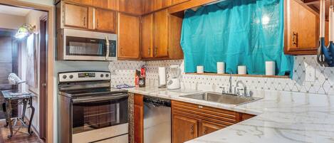 A kitchen with wooden cabinets, stainless steel appliances, a tiled backsplash, and a marble countertop.