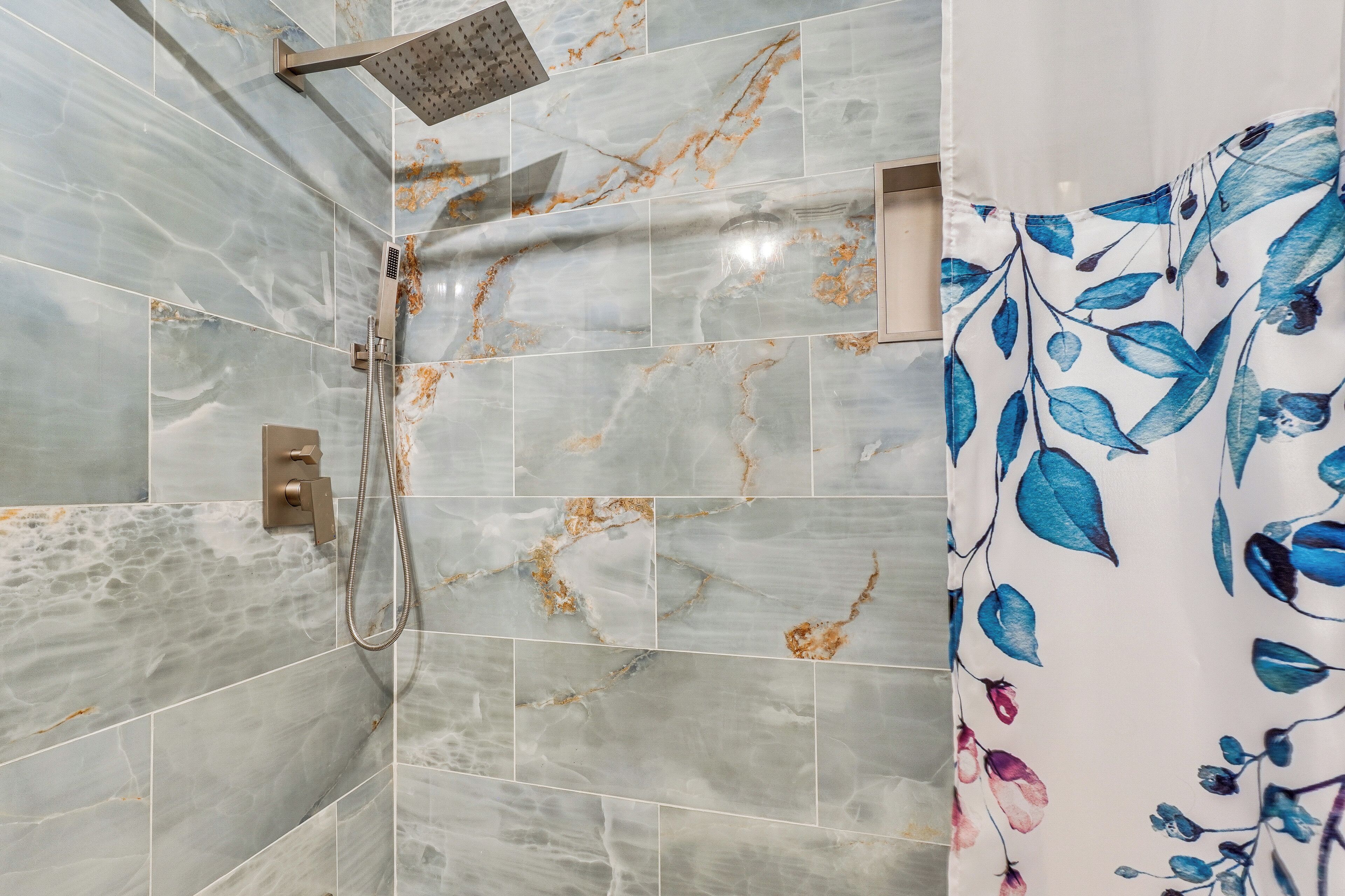 Une salle de bain carrelée de marbre, avec une douche et un rideau à motifs floraux.