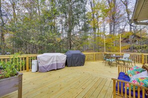 Eine Holzterrasse mit Gartenmöbeln, einem überdachten Grill und einer überdachten Mülltonne.