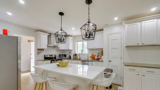 Una cocina moderna con armarios blancos, una isla central con taburetes y luminarias colgantes.