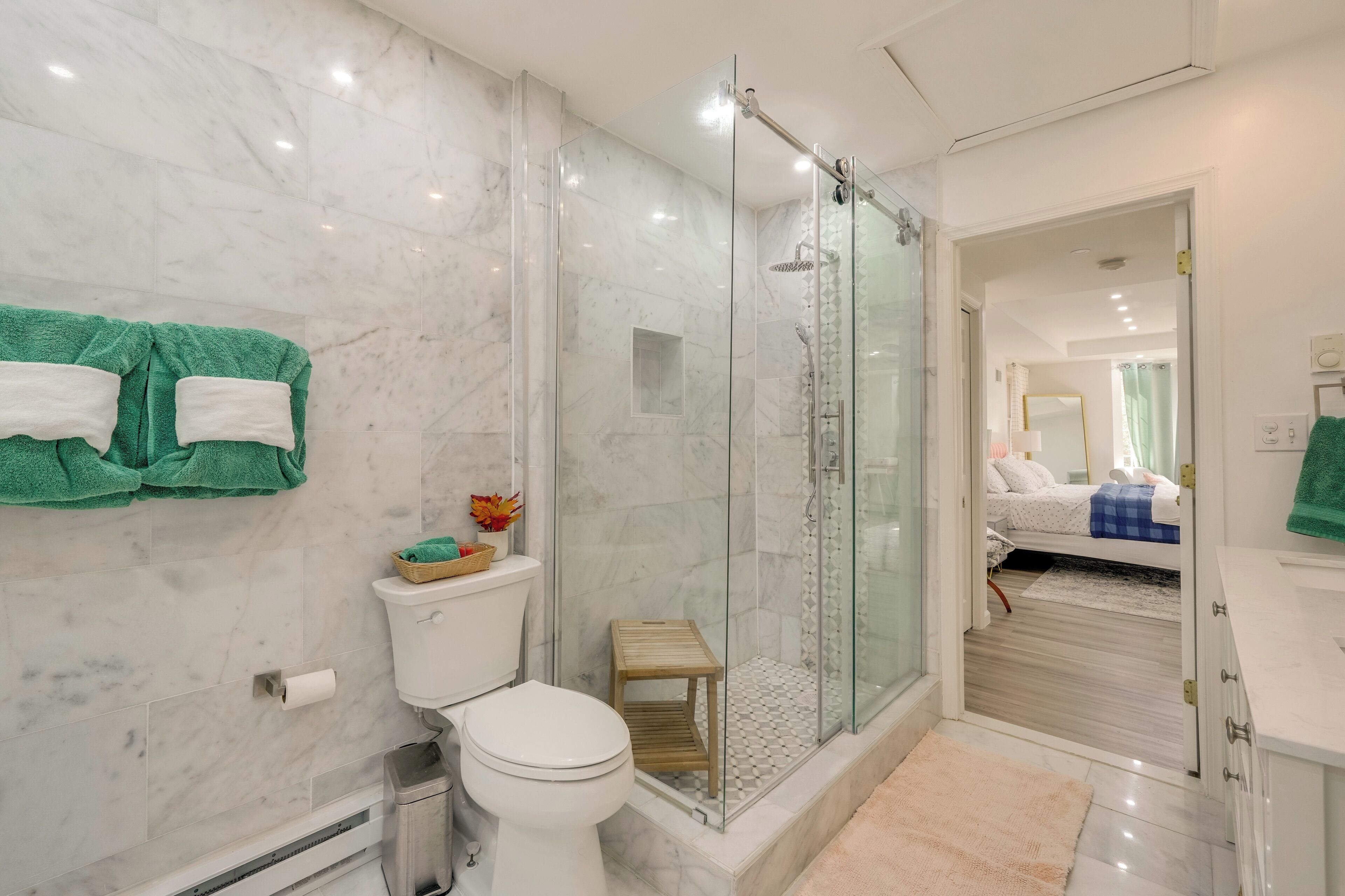 A modern bathroom with a glass-enclosed shower, a toilet, and a small wooden stool.