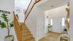 Una escalera que lleva al segundo piso, paredes blancas y una puerta con una pequeña planta a su lado.