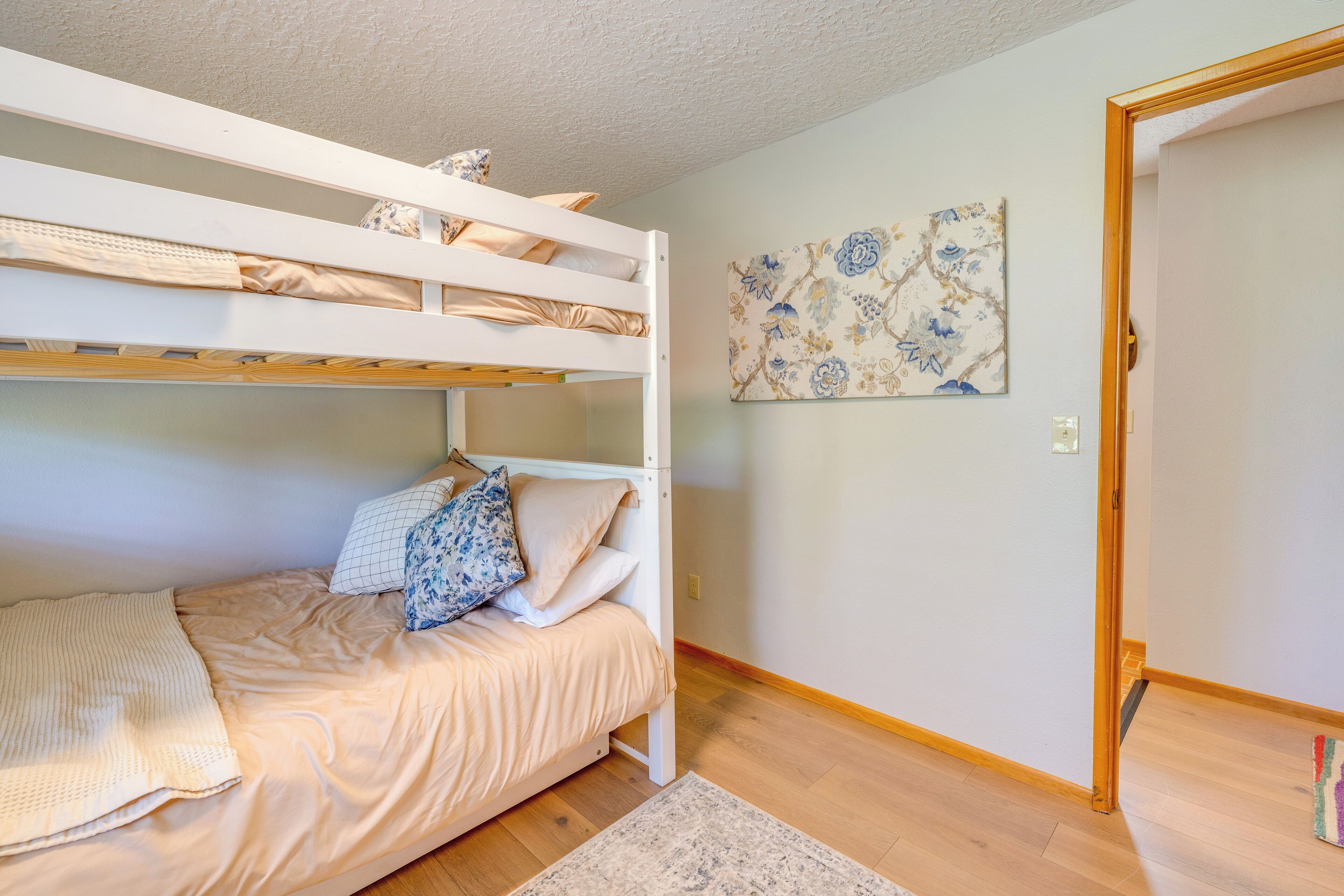A bunk bed room with a wooden floor, a patterned rug, and a floral wall art piece.