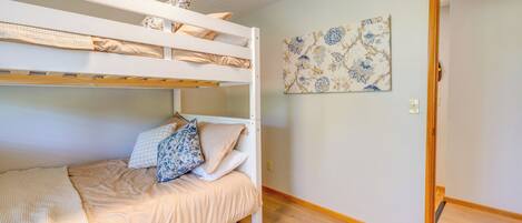 A bunk bed room with a wooden floor, a patterned rug, and a floral wall art piece.