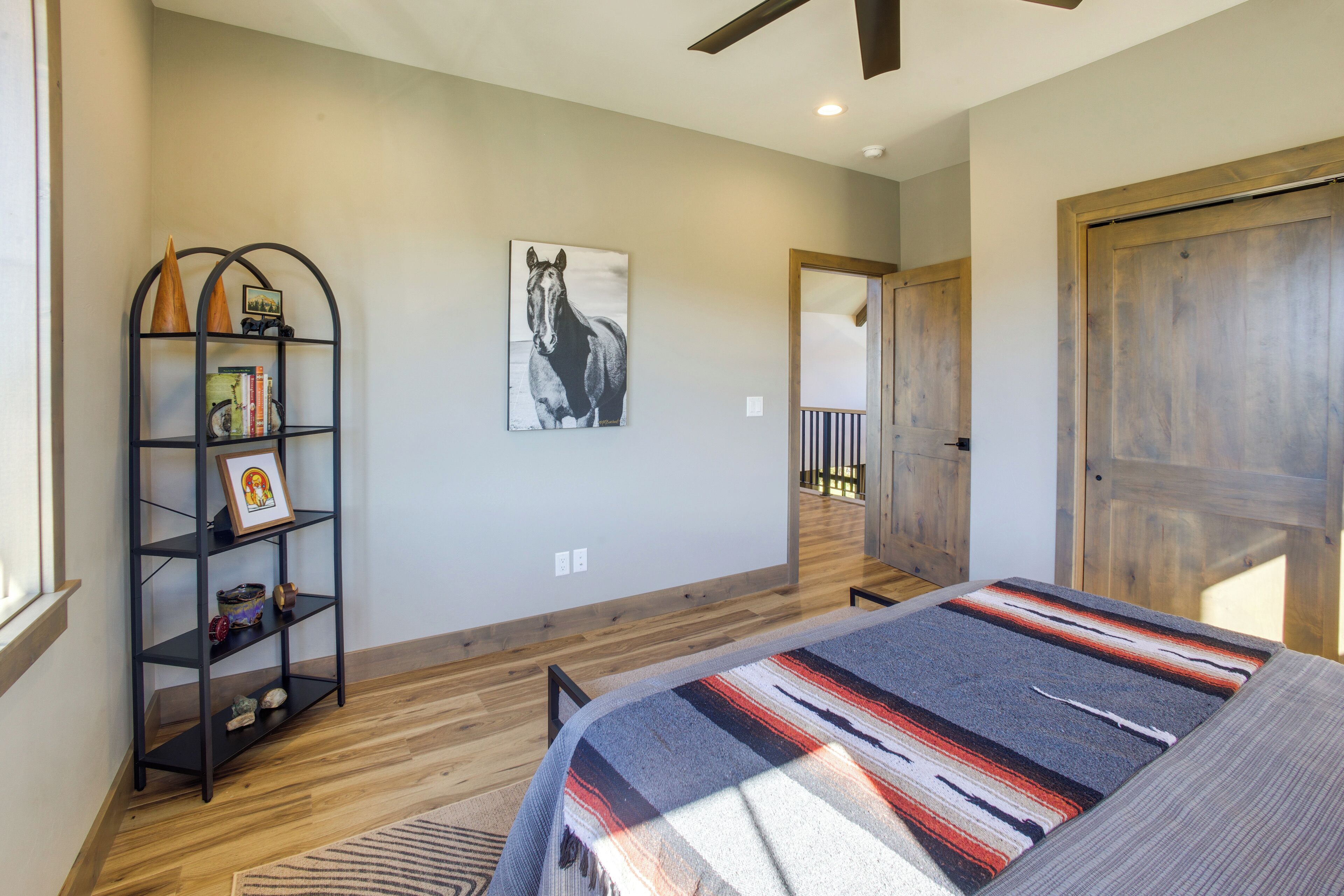 A bedroom with a bed, a bookshelf, a framed picture, and a horse painting on the wall.