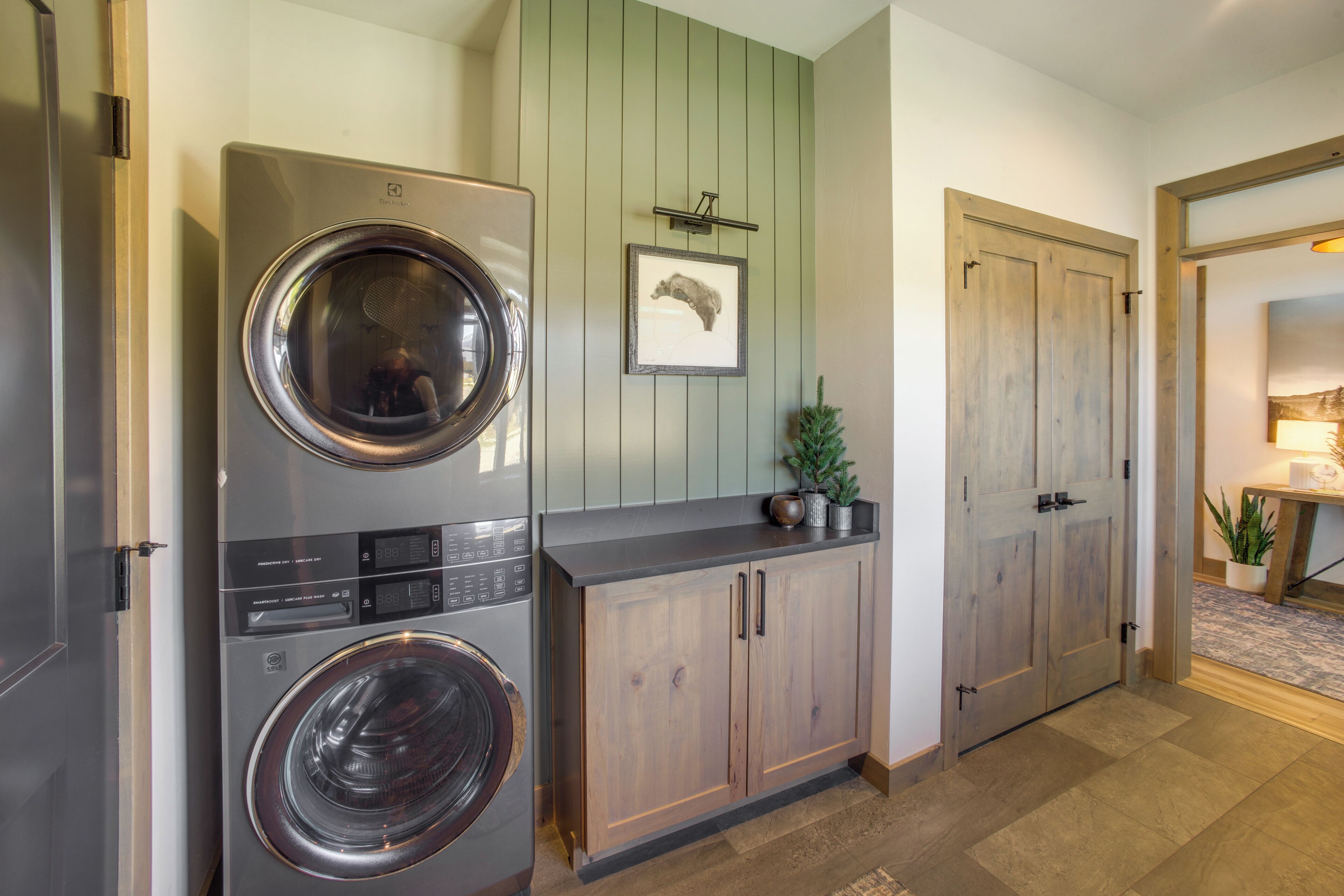 A laundry room with a front-loading washer and dryer, wooden cabinets, and a green wall with a framed picture.