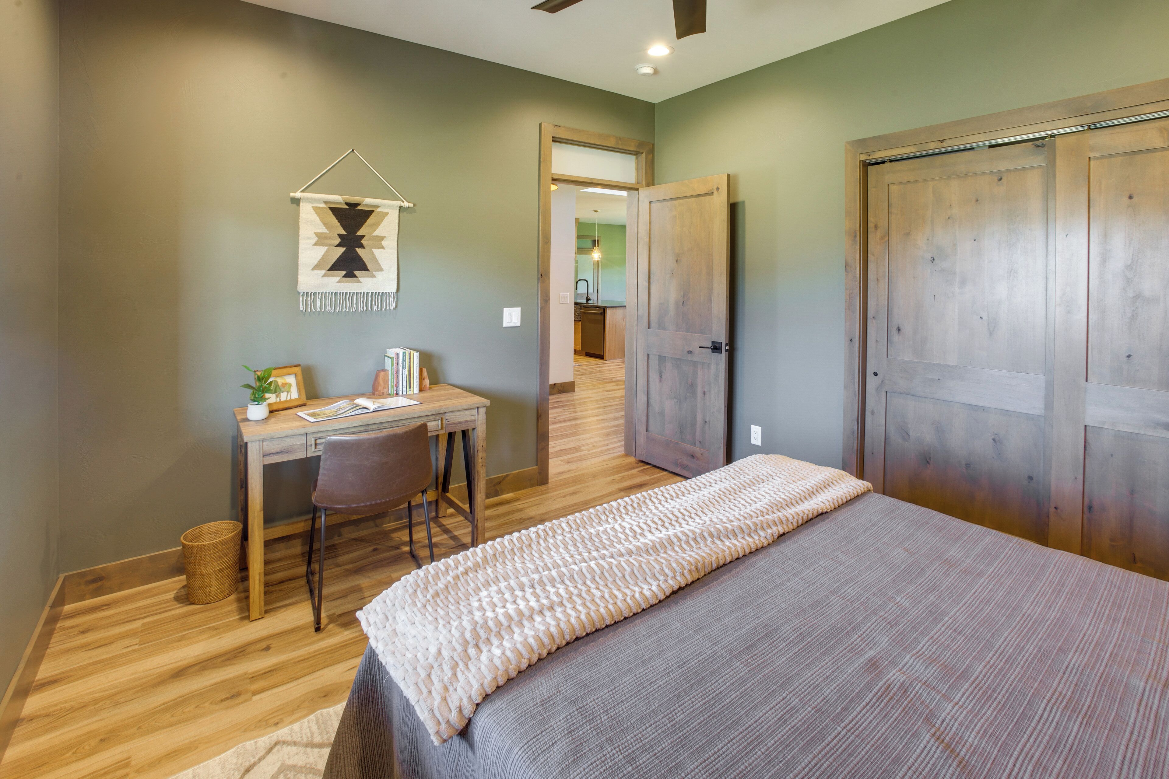 A bedroom with a bed, a desk, and a chair. There is a door leading to another room.
