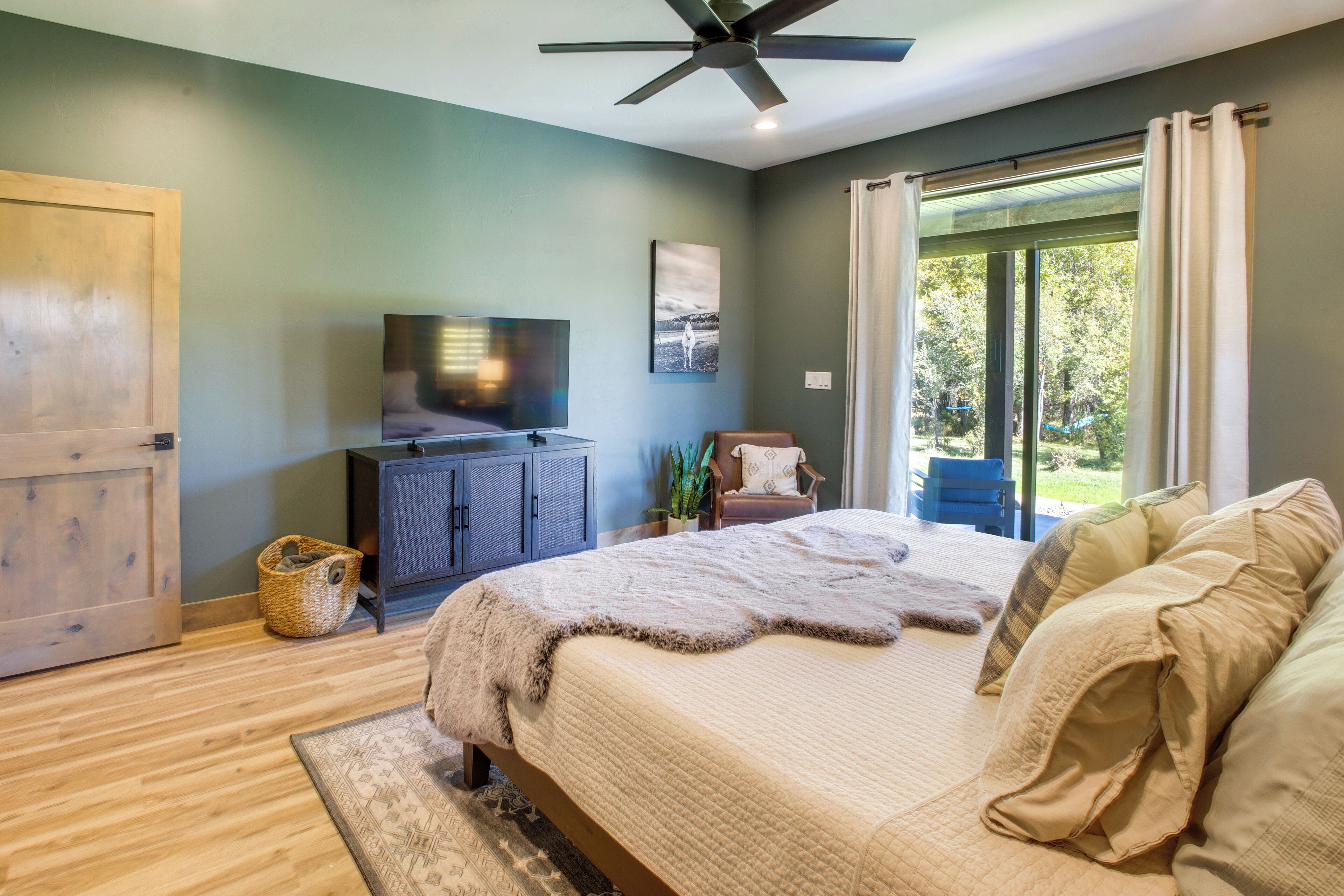 A bedroom with a bed, a TV, a wooden door, and a window with curtains.