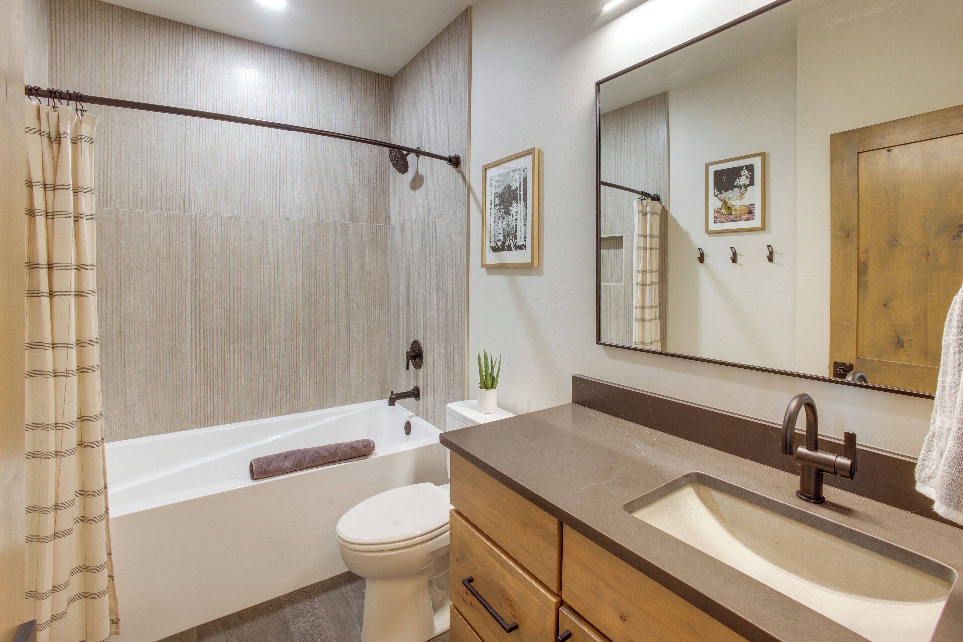 A bathroom with a bathtub, toilet, vanity with drawers, a sink, and a large mirror.