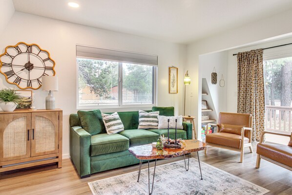 A living room with a green sofa, a wooden cabinet, a coffee table, and a large window with curtains. - Rim Country Retreat: A-frame Cabin w/ Large Deck (Overgaard)