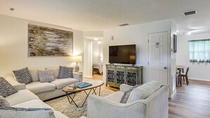 A living room with a sofa set, a coffee table, a TV on a cabinet, and a painting on the wall. - Game Room, Yard: Home 3 Mi to Daytona Beach! (Holly Hill)