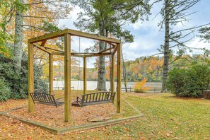 A wooden gazebo with benches, surrounded by trees and a lake.