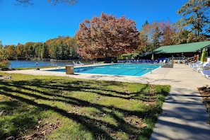 A swimming pool with lounge chairs and a covered area, surrounded by trees and a lake.
