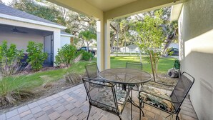 A covered patio with a round metal table and four chairs, surrounded by a brick patio and small plants.