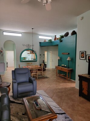 Un salon spacieux avec un fauteuil bleu, une table basse en verre et un coin repas comprenant une table et des chaises en bois.