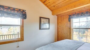 A bedroom with wooden walls and ceiling, a bed with a gray blanket, a framed picture on the wall, and a window with a view of trees. - Private Wooded Escape w/ Scenic Decks in Jefferson (Jefferson)