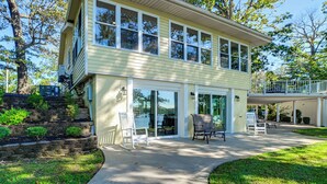 A two-story house with a patio area, large windows, and a covered deck. - Spacious Kentucky Lake Escape w/ Dock & Views (Benton)