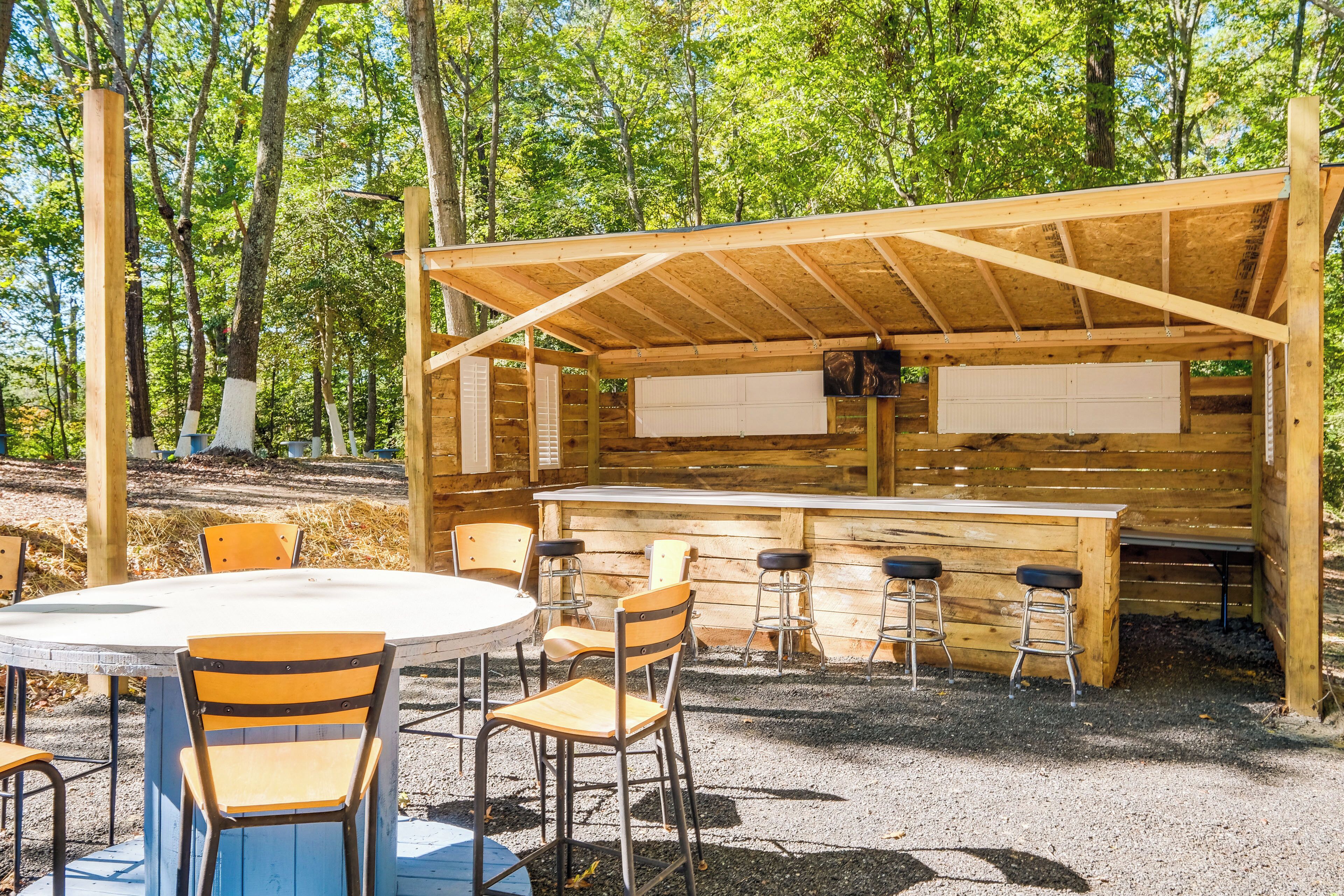 An outdoor wooden structure with a bar area, round table, and chairs.