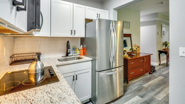 A modern kitchen with white cabinets, stainless steel appliances, and a marble countertop.