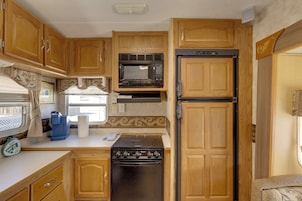 Cocina compacta para vehículos recreativos con armarios de madera, estufa, microondas y refrigerador.