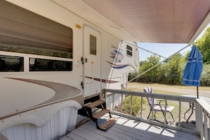 Un espacio cubierto con una caravana blanca, una sombrilla azul y una silla.