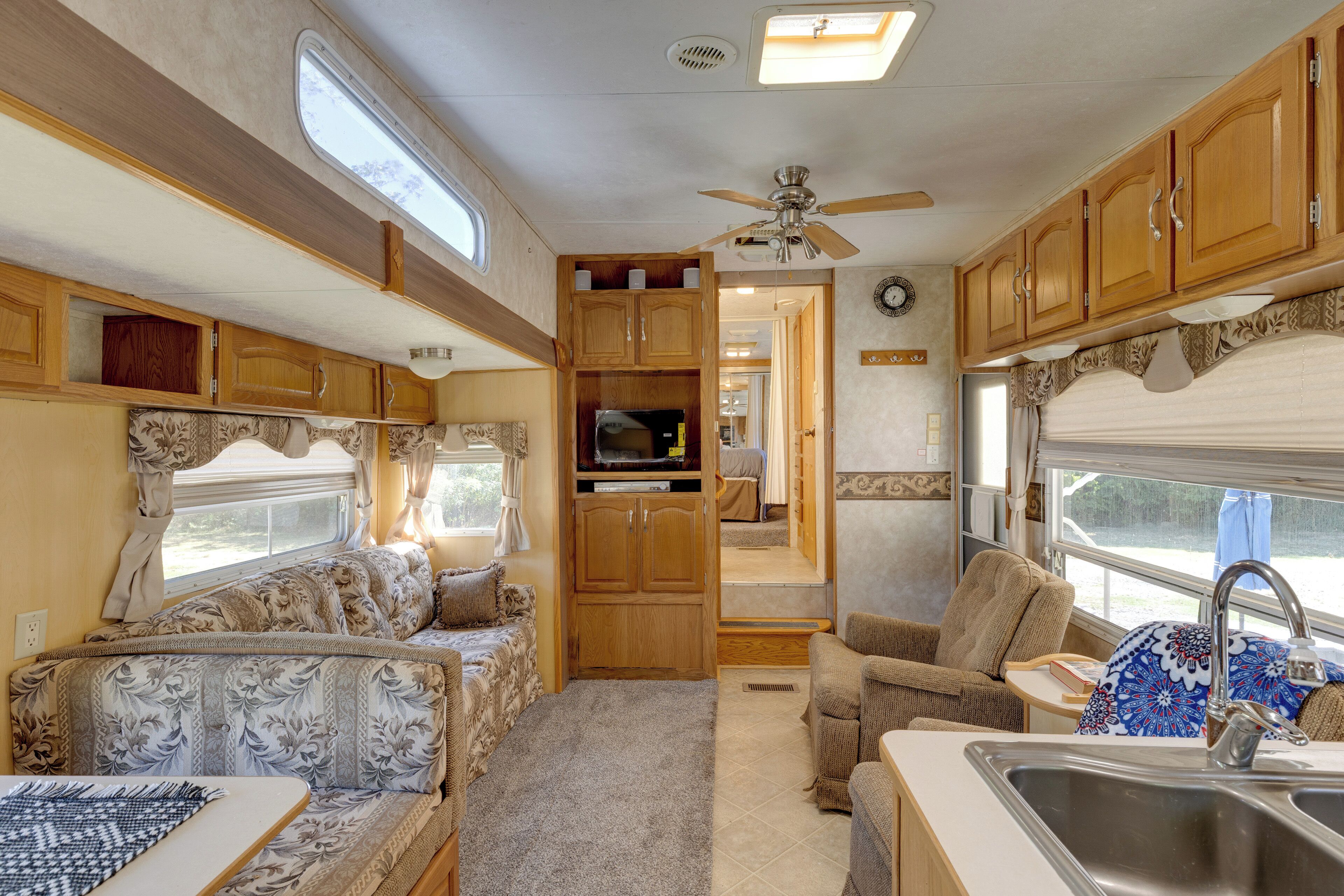 A compact RV interior with a kitchenette, seating area, and a ceiling fan.