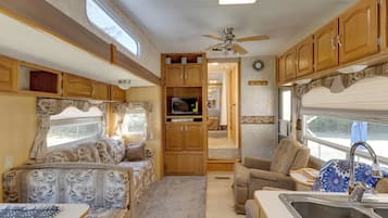 A compact RV interior with a kitchenette, seating area, and a ceiling fan.