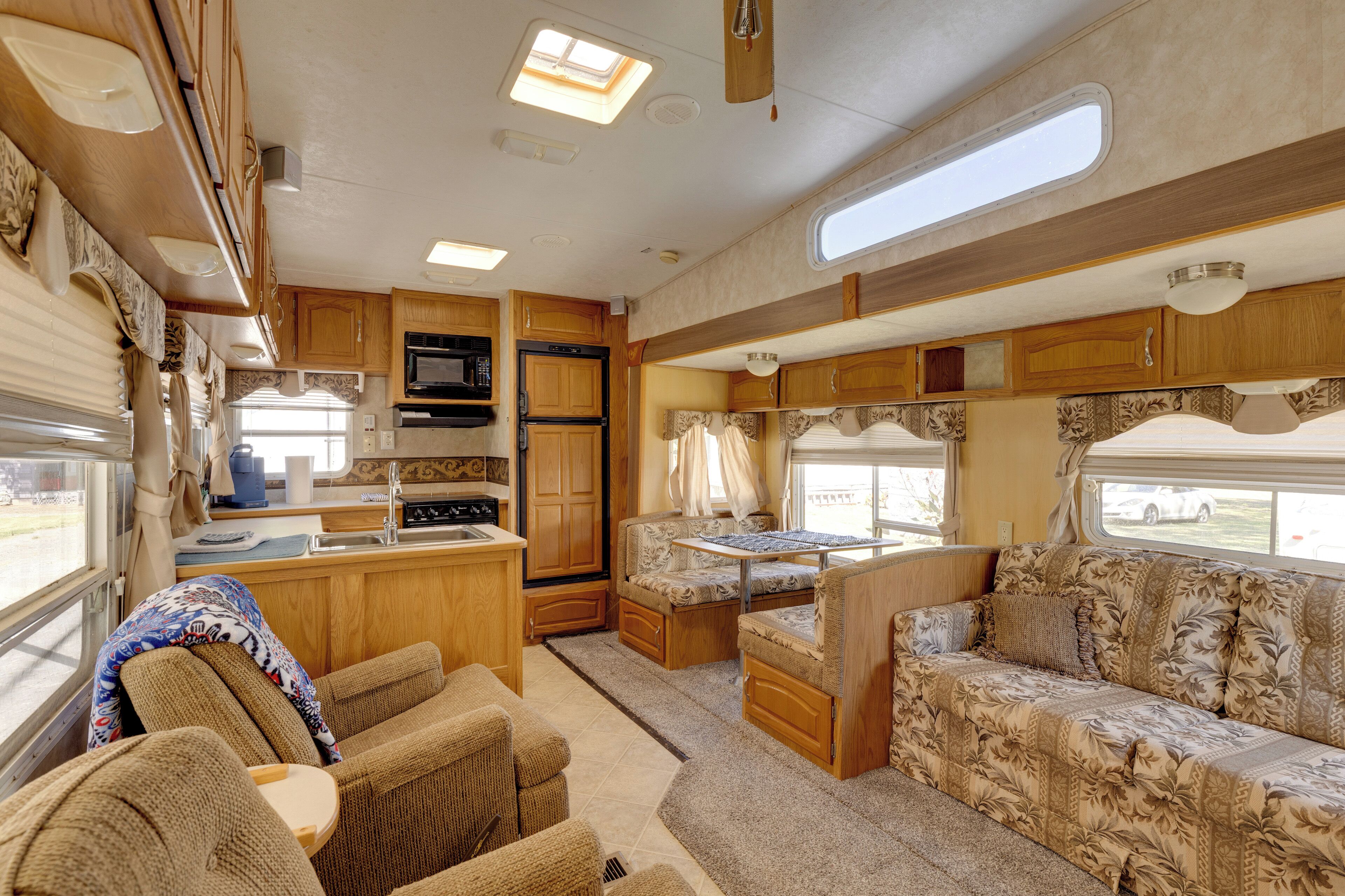 A compact RV interior with a kitchenette, a dining area, and a seating area with a sofa and chairs.