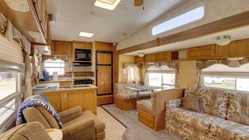 A compact RV interior with a kitchenette, a dining area, and a seating area with a sofa and chairs.