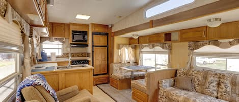 Ein kompaktes Wohnmobil-Interieur mit einer Küchenzeile, einem Essbereich und einer Sitzecke mit Sofa und Sesseln.