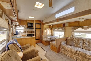 A compact RV interior with a kitchenette, a dining area, and a seating area with a sofa and chairs. - 2 Mi to Lake Guntersville: Peaceful Camper Home (Langston)
