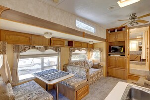 Interior compacto de una caravana con kitchenette, zona de comedor y espacio de estar con cortinas.