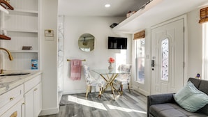 A modern kitchen with white cabinetry, a marble countertop, and a glass dining table with two chairs. - Solo Escape w/ Hot Tub! 10 Mi to Dtwn Sacramento (Rio Linda)