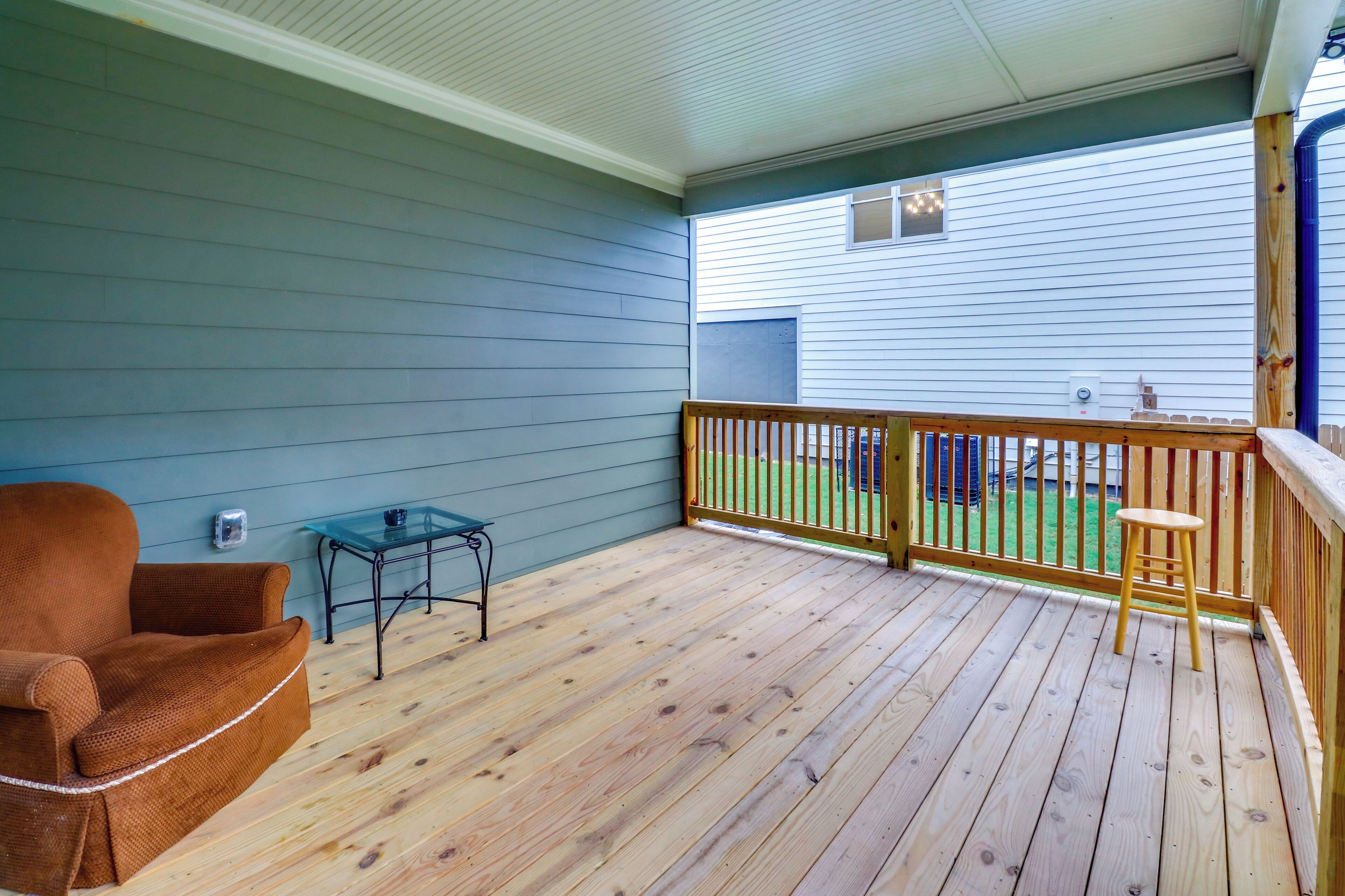 A covered porch with a wooden deck, a brown chair, a small table, and a railing.